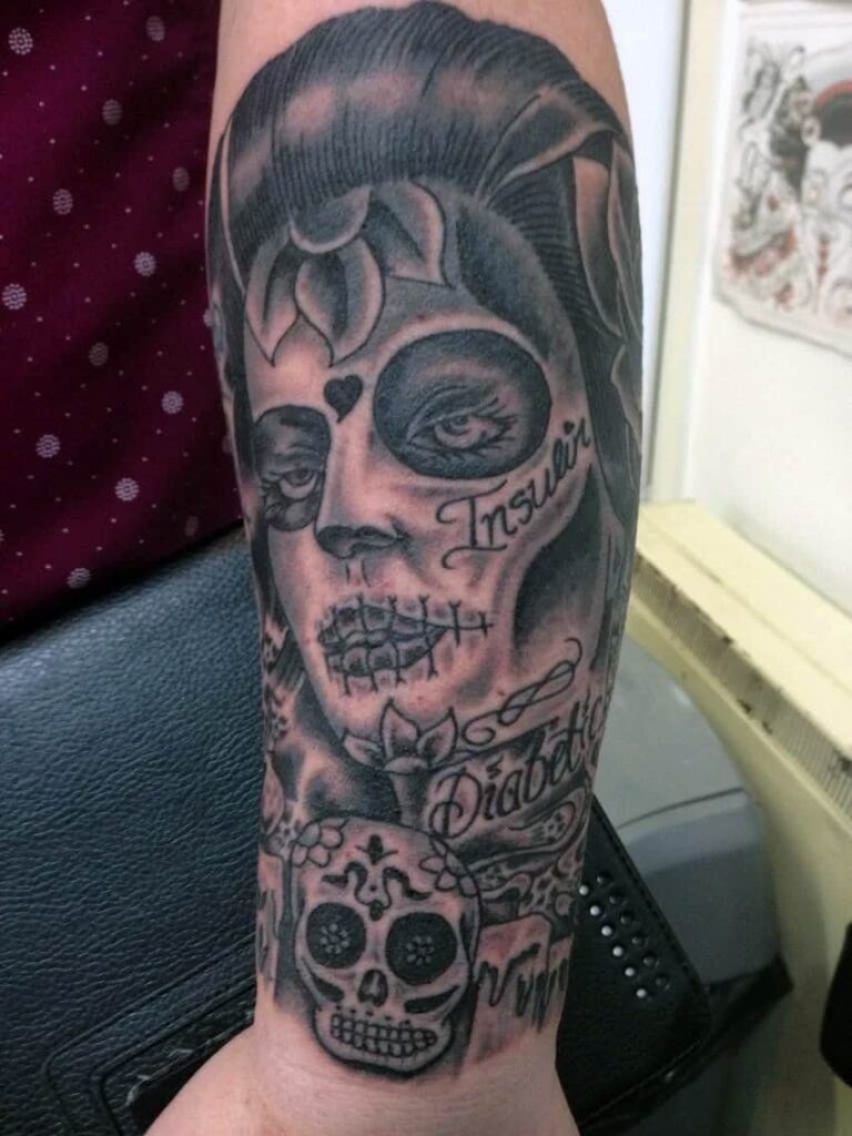 Mexican style day of the dead face with sugar skull and text. Lower arm. John at Rogsy Tattoo Studio.